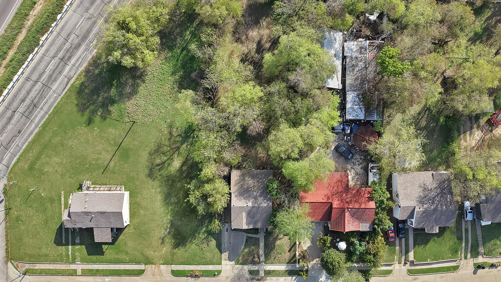 Aerial view of residential property featuring a sprawling corner lot, mature trees, concrete driveway, and established lawn