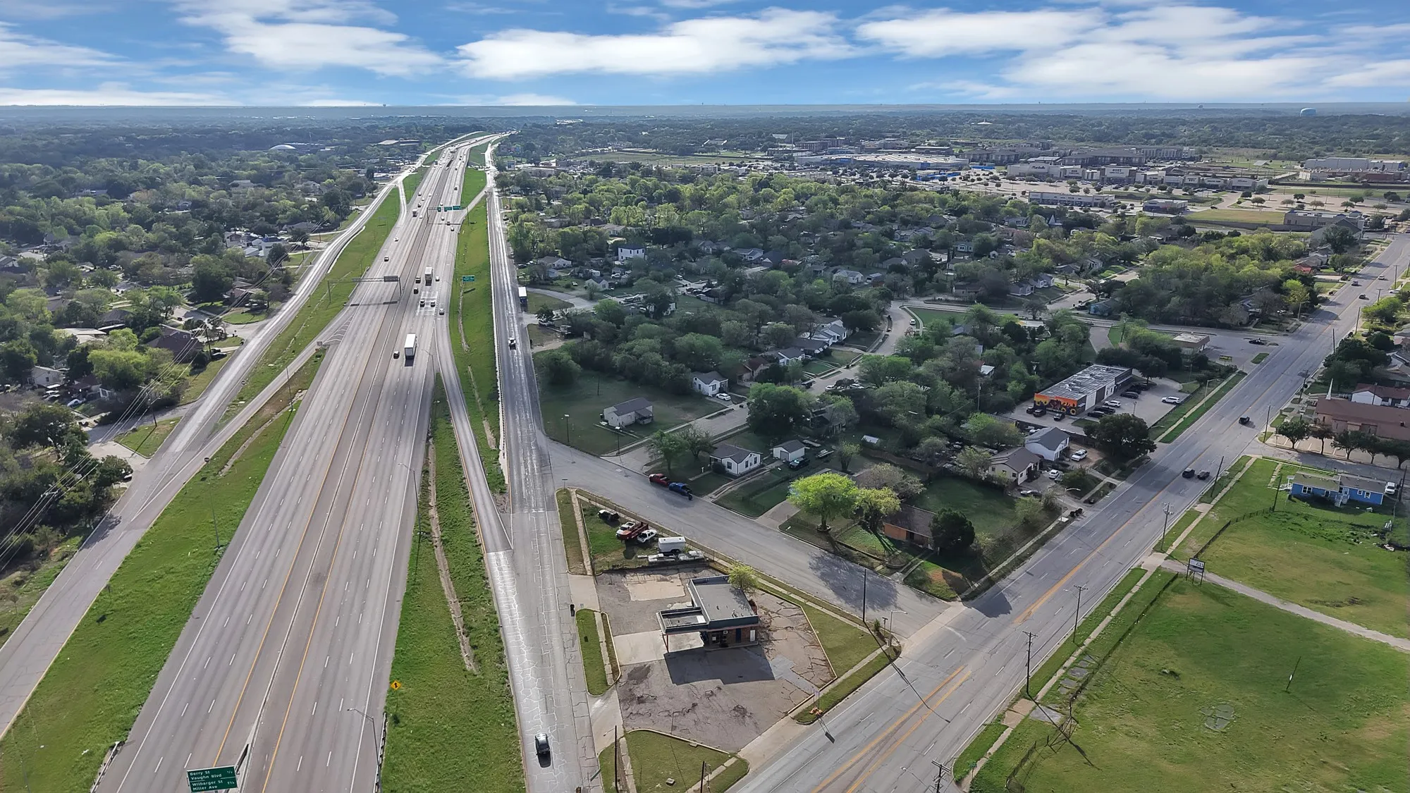 Aerial perspective of the surrounding area featuring multi-lane highway infrastructure, commercial properties, and established residential neighborhoods with mature tree canopy coverage