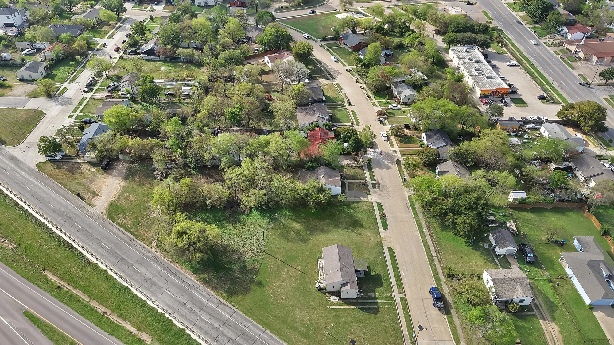 Aerial perspective showcasing a residential lot with mature trees situated in a suburban neighborhood near local thoroughfares
