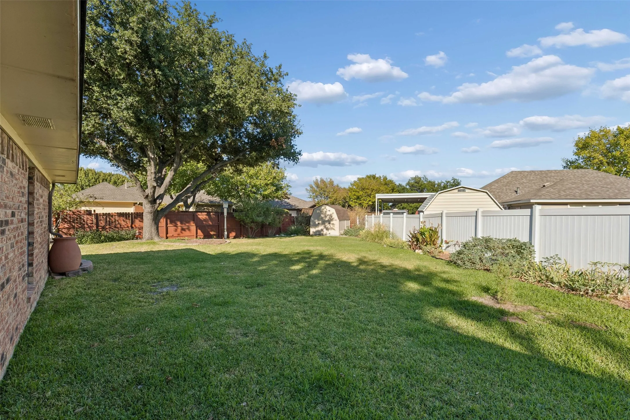 Backyard featuring an expansive lawn, mature tree, brick exterior wall, and perimeter fencing