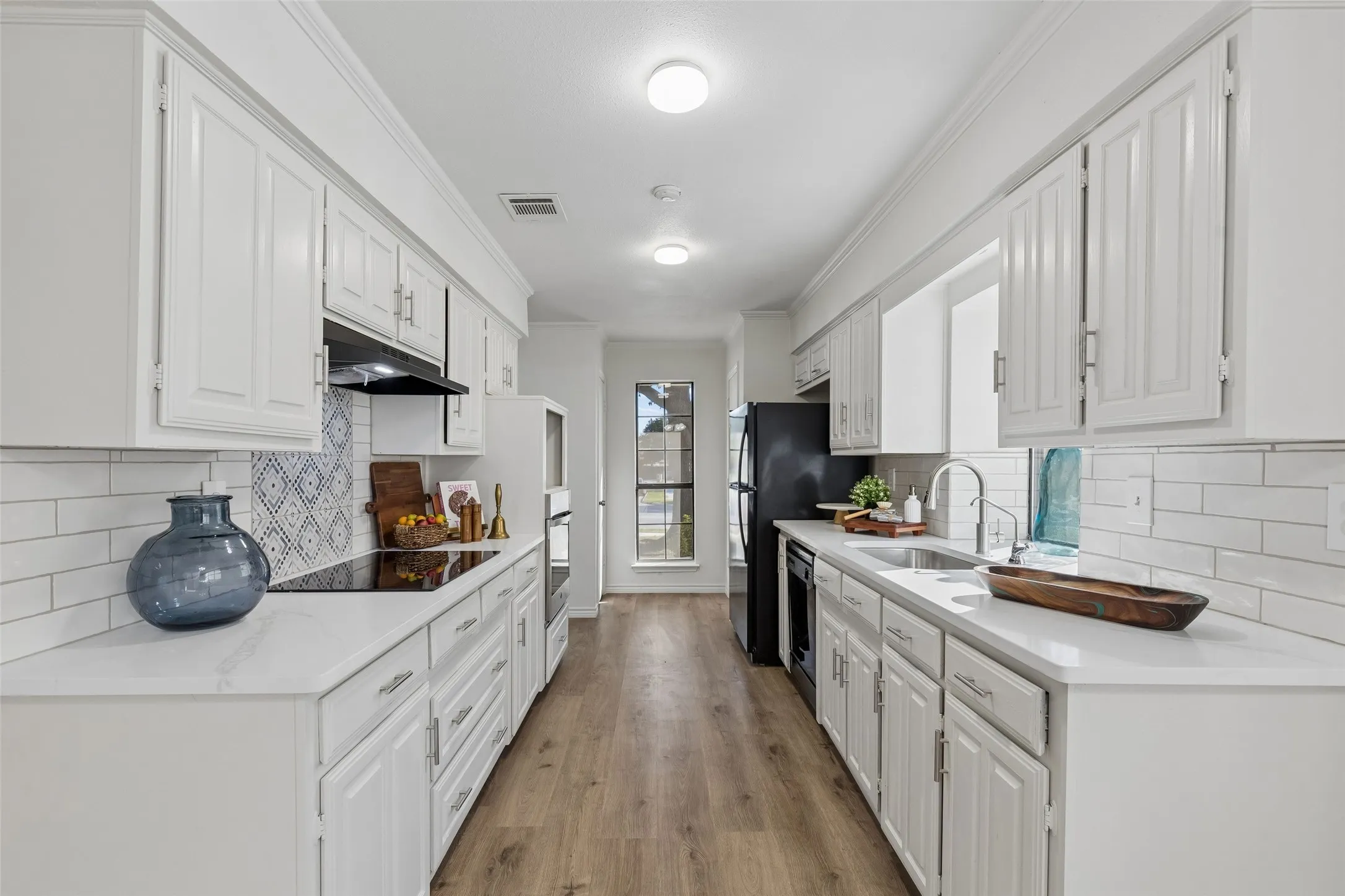 Galley kitchen featuring white shaker-style cabinetry, quartz countertops, white subway tile backsplash, patterned tile accent, and wood-finish flooring