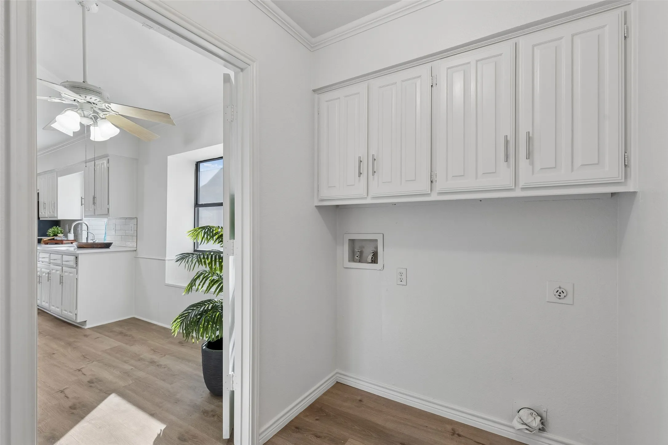 Utility area featuring white raised-panel cabinetry, wood-finish flooring, and dedicated laundry hookups