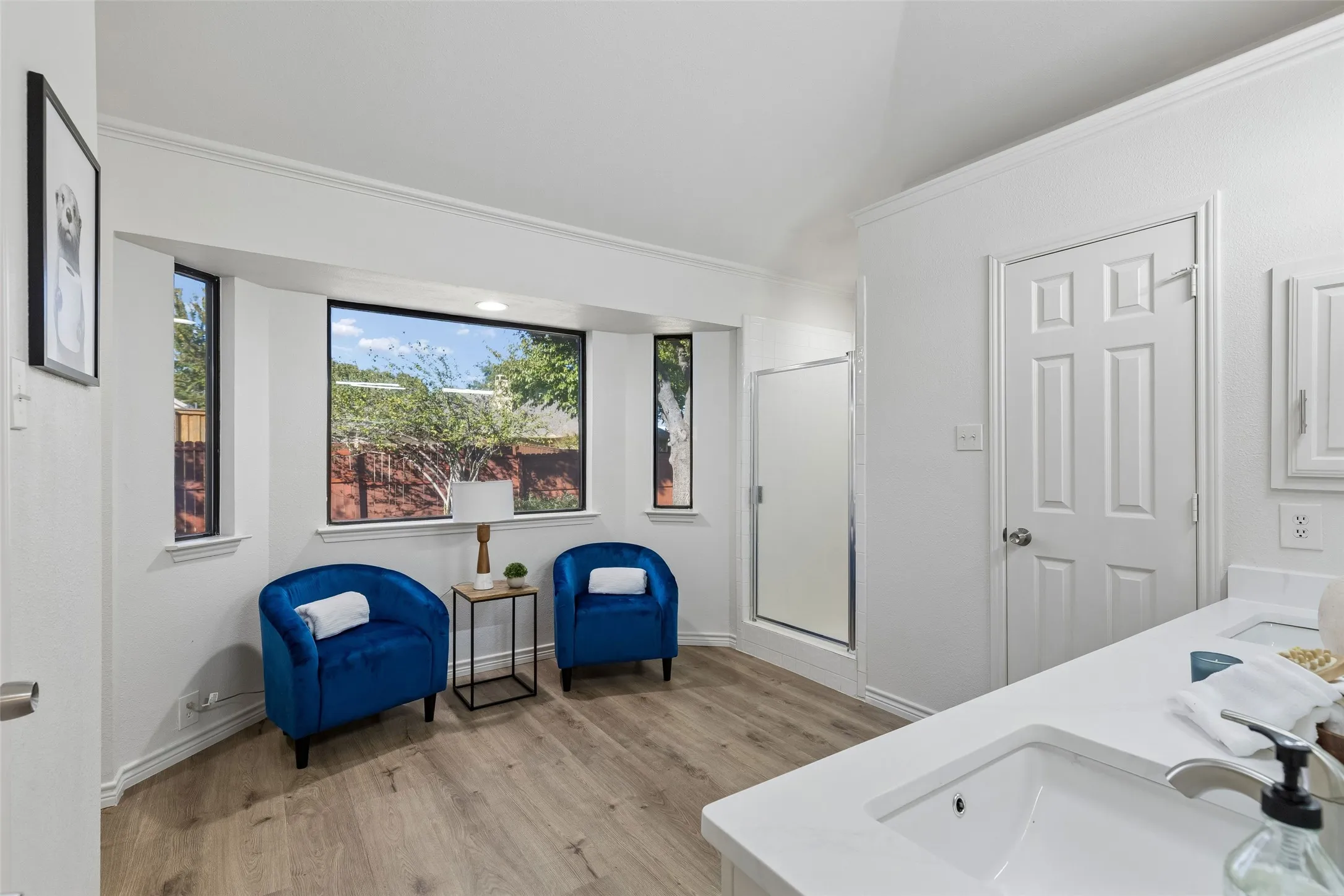 Bathroom interior featuring wood-finish flooring, a double-sink vanity with white countertop, vaulted ceilings, and a bay window configuration