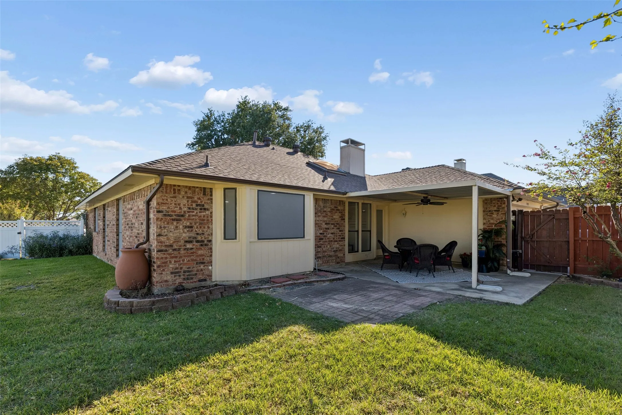 Brick exterior featuring a covered patio, paved hardscaping, a stone-bordered garden bed, and a wooden privacy fence