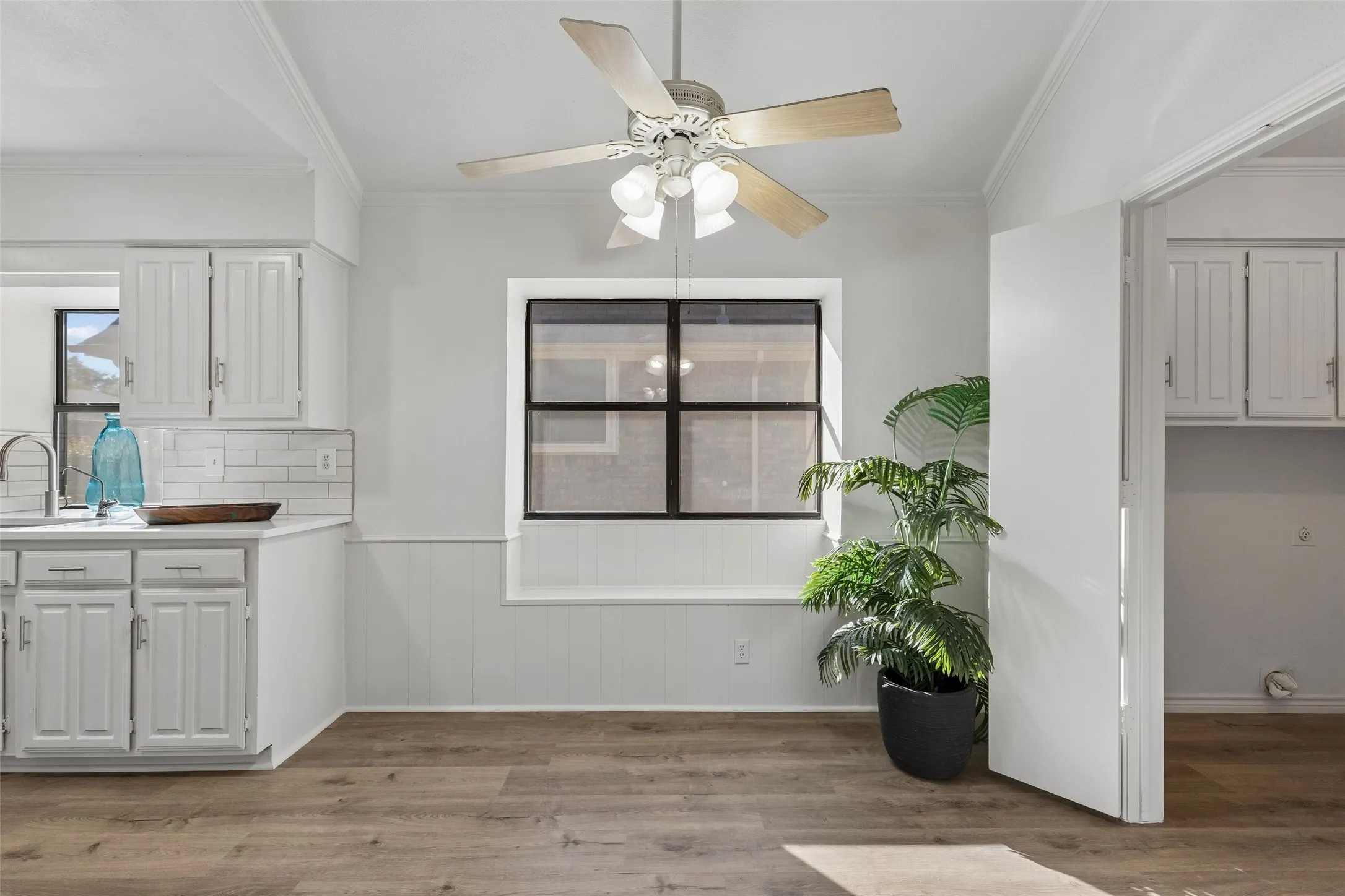 Eat-in area featuring wood-finish flooring, a built-in window seat, white wainscoting, and a ceiling fan with integrated lighting