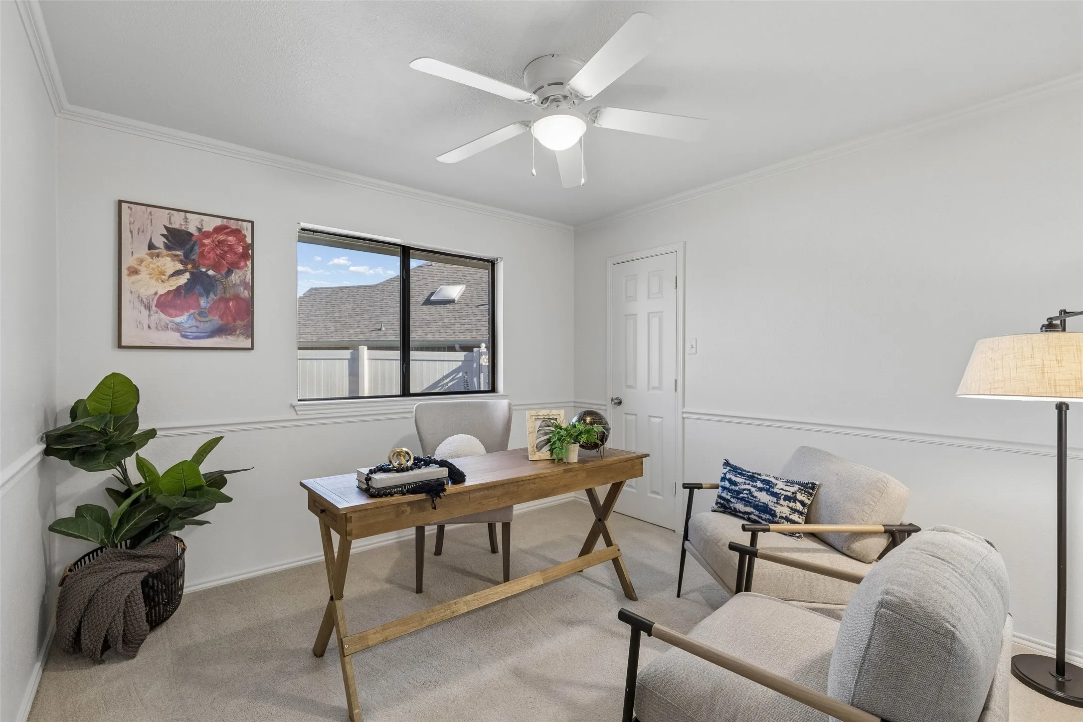 Neutral-toned room featuring crown molding, wainscoting, carpeted flooring, a ceiling fan with integrated lighting, and a single-pane window