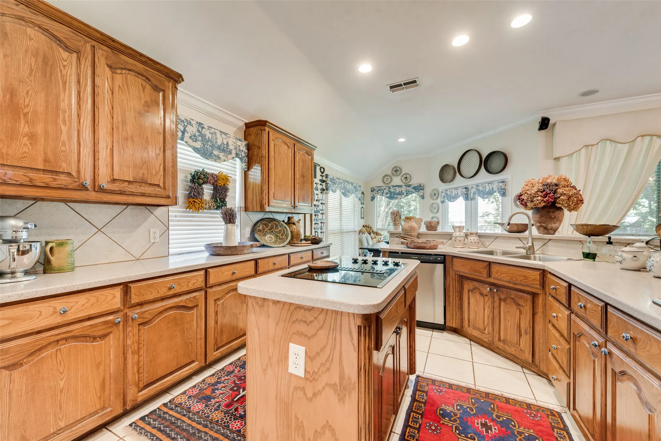 Kitchen featuring stained wood cabinetry, stone-finish countertops, diagonal tile backsplash, center island with an integrated cooktop, and tile flooring