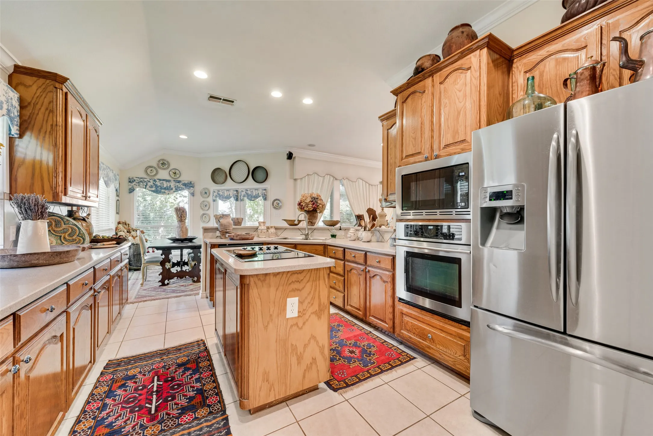 Kitchen featuring custom wood cabinetry, stainless steel appliances, a center island with a cooktop, and neutral tile flooring