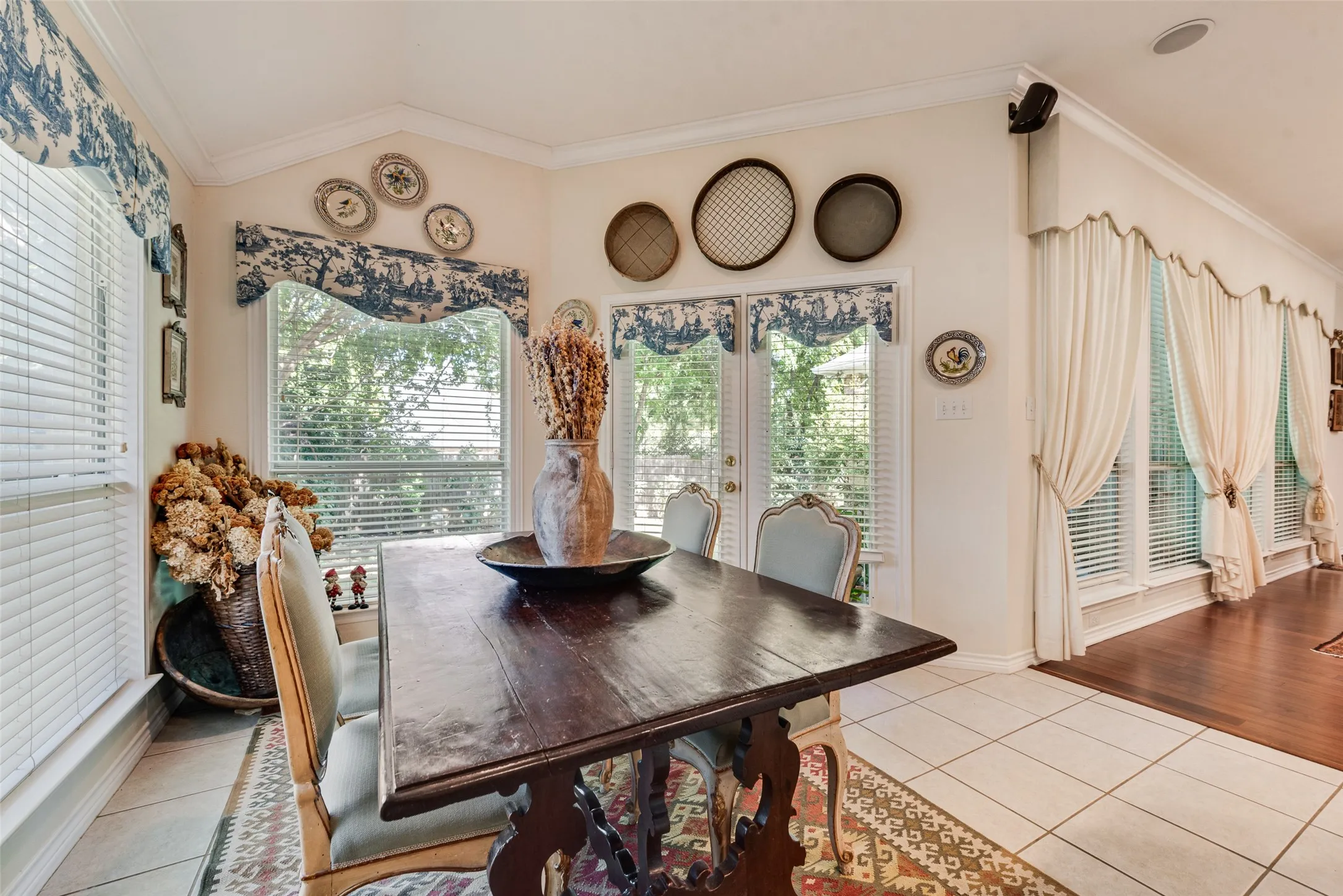 Sun-drenched dining area featuring vaulted ceilings, oversized windows with crown molding, double glass doors with exterior access, and ceramic tile flooring