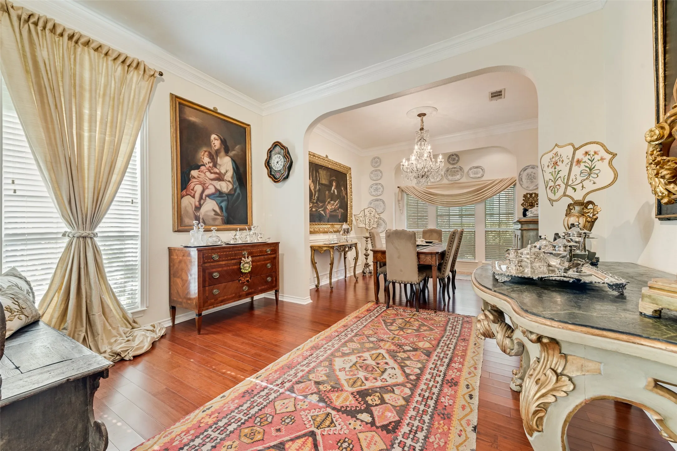 Wood-finish flooring, crown molding, arched entry, and ornate crystal chandelier