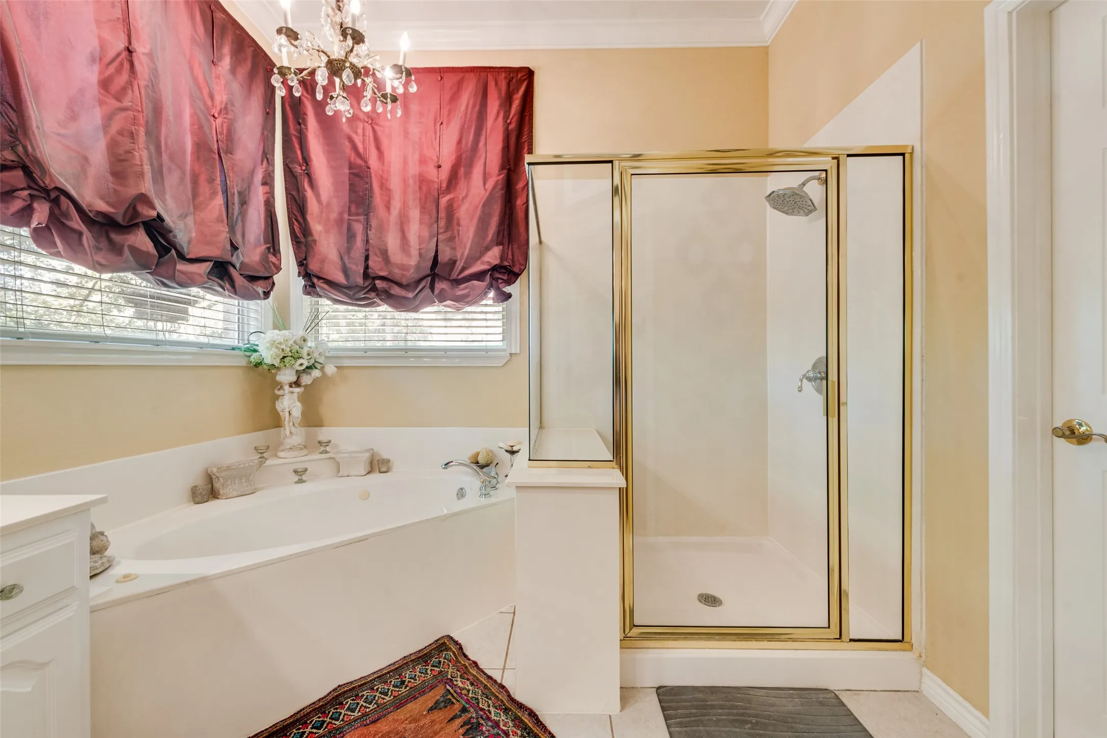 Jetted soaking tub, separate glass-enclosed shower with gold-tone metal framing, and tiered chandelier lighting