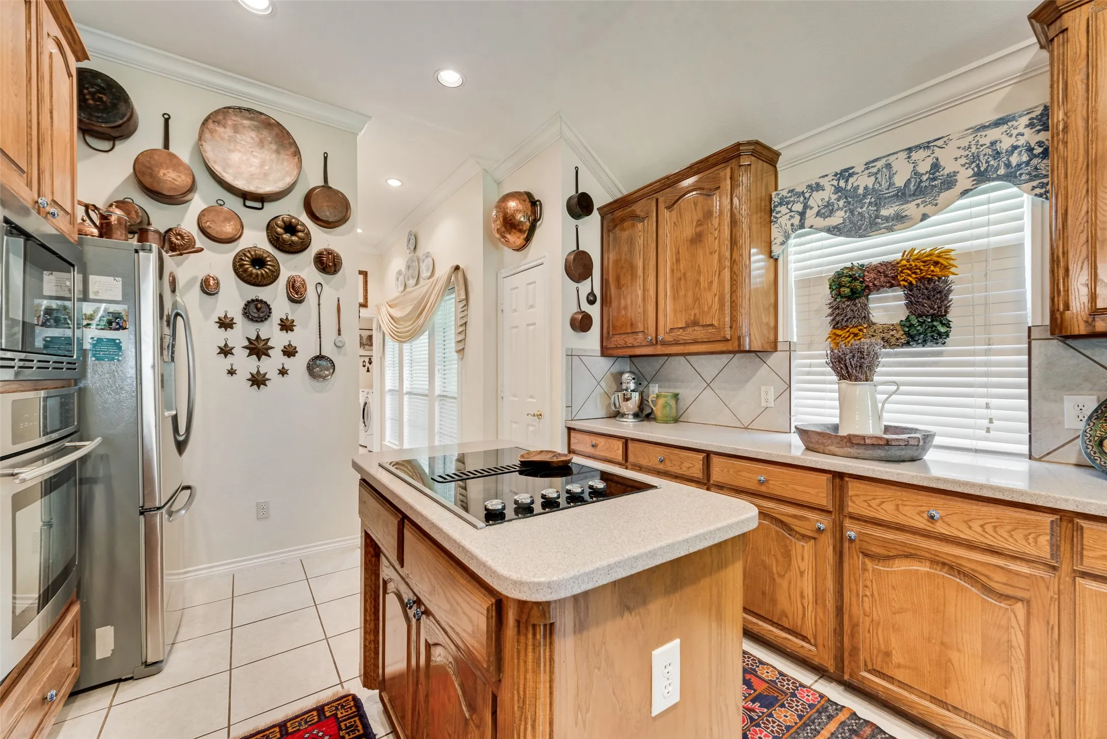 Kitchen featuring natural wood cabinetry, central island with an integrated cooktop, stone-composite countertops, stainless steel wall-mounted oven, and ceramic tile flooring