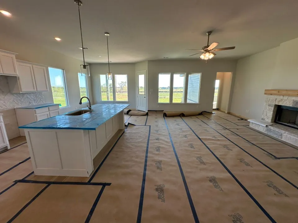 Kitchen featuring a central island with a sink, white cabinetry, herringbone-patterned tile backsplash, pendant lighting, and a stone-clad fireplace with a timber mantel