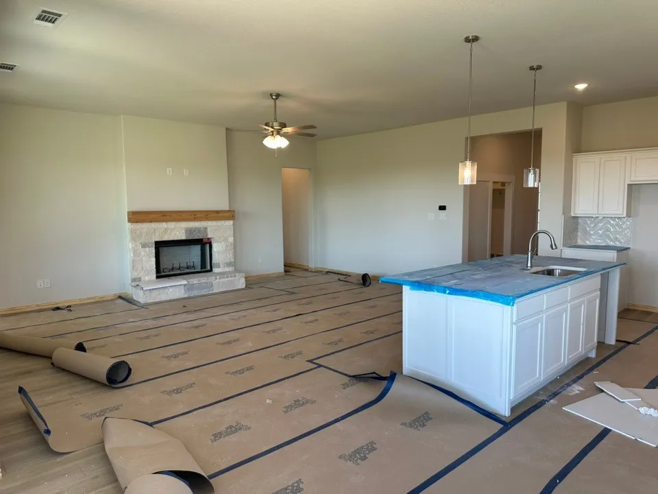 Open-concept layout featuring a stone-faced fireplace with a wood mantel, a central kitchen island with an undermount sink, white shaker-style cabinetry, and pendant lighting