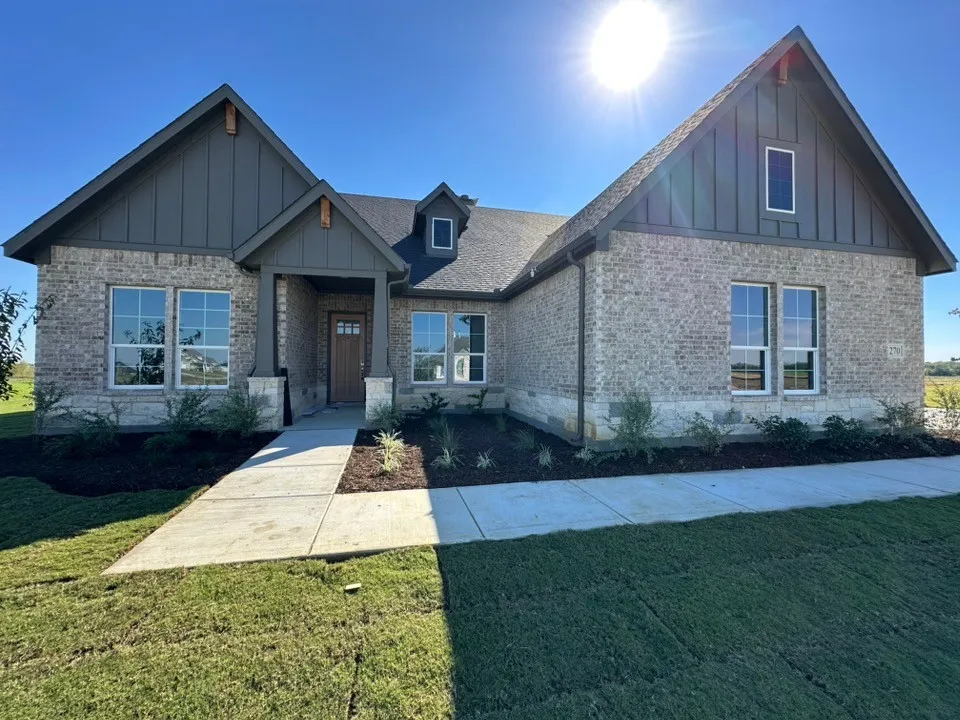 Exterior facade featuring multi-tone brick and stone masonry, board and batten siding, high-pitched gable rooflines, and a concrete walkway