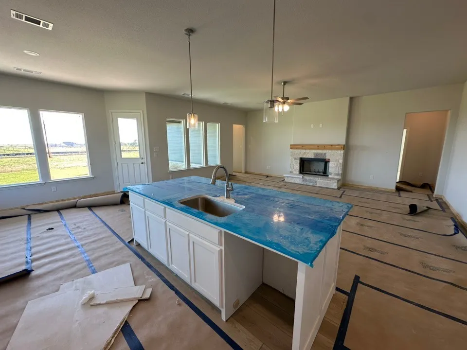 Kitchen island with stone-finish countertop, undermount sink, and pendant lighting, complemented by a floor-to-ceiling stone fireplace featuring a wood mantel