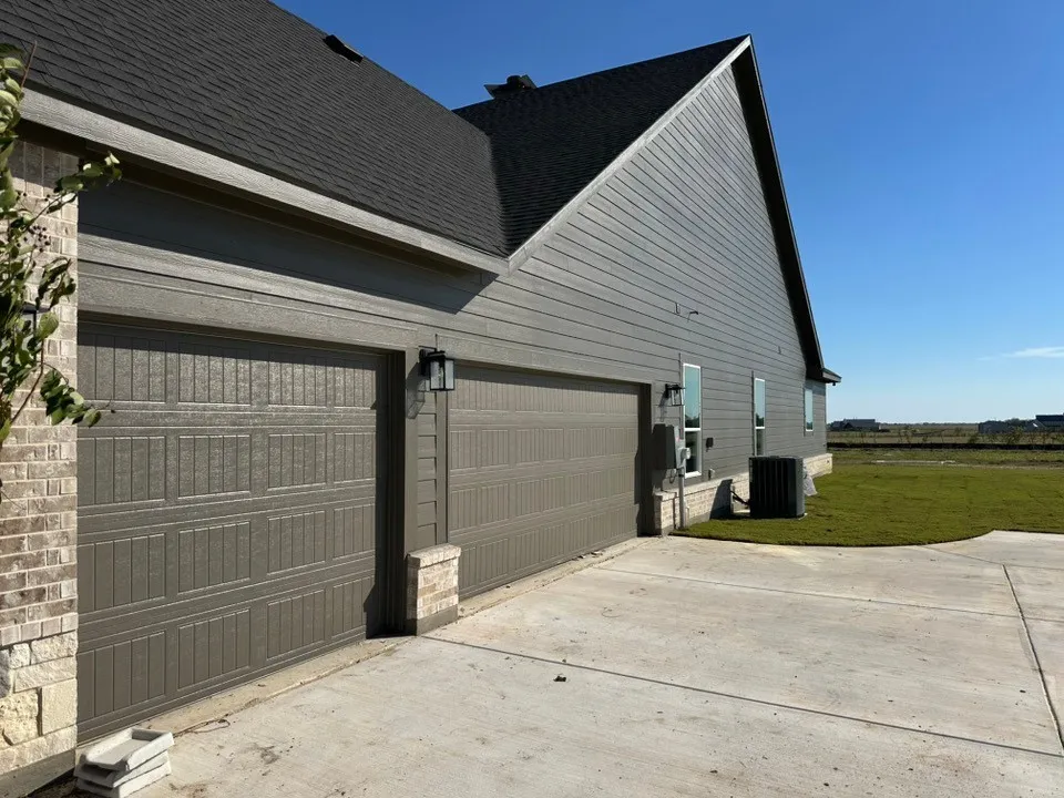 Exterior featuring horizontal lap siding, multi-car garage with paneled doors, stone veneer accents, asphalt shingled roof, and a concrete driveway