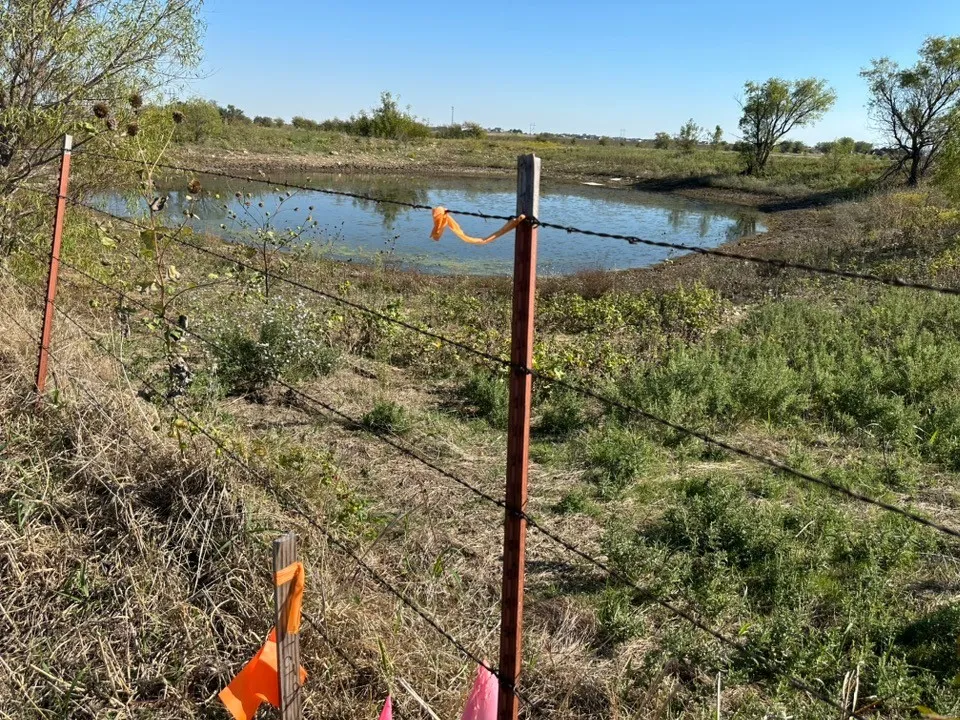 Natural pond situated on acreage, enclosed by a wire fence with metal posts