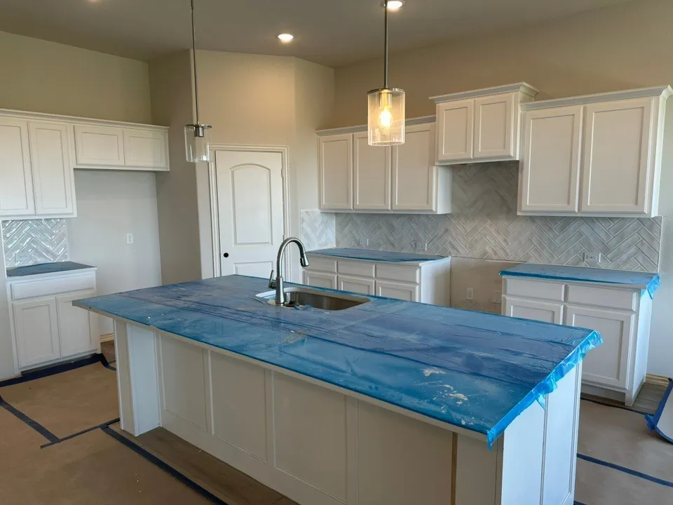 Kitchen featuring white shaker-style cabinetry, central island with undermount sink, herringbone-patterned tile backsplash, and two glass pendant lights