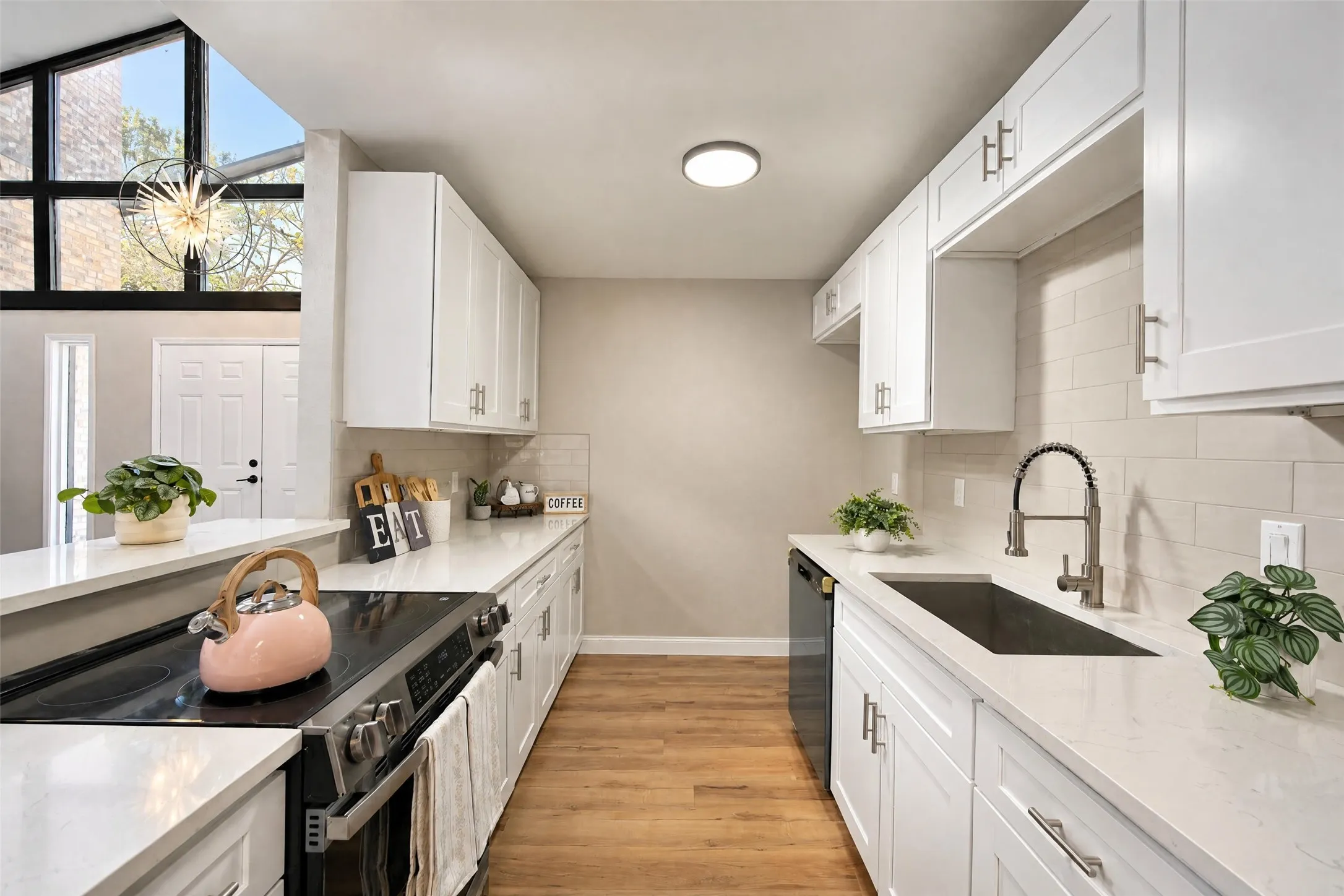 Kitchen featuring white shaker-style cabinetry, quartz countertops, subway tile backsplash, stainless steel sink with high-arc faucet, and wood-finish flooring