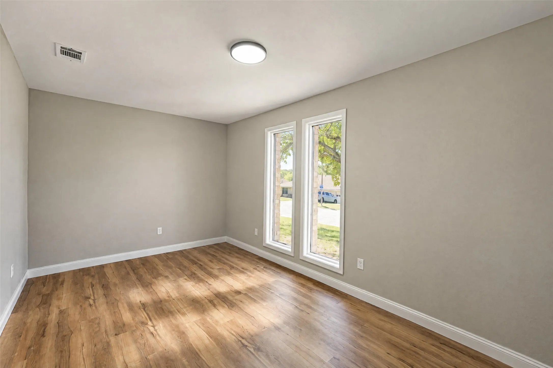 Neutral-toned walls paired with wood-finish flooring and dual tall windows featuring white trim
