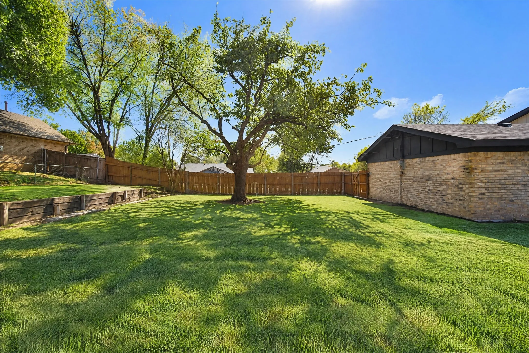Backyard featuring a manicured lawn, mature trees, wooden privacy fencing, and tiered timber retaining walls