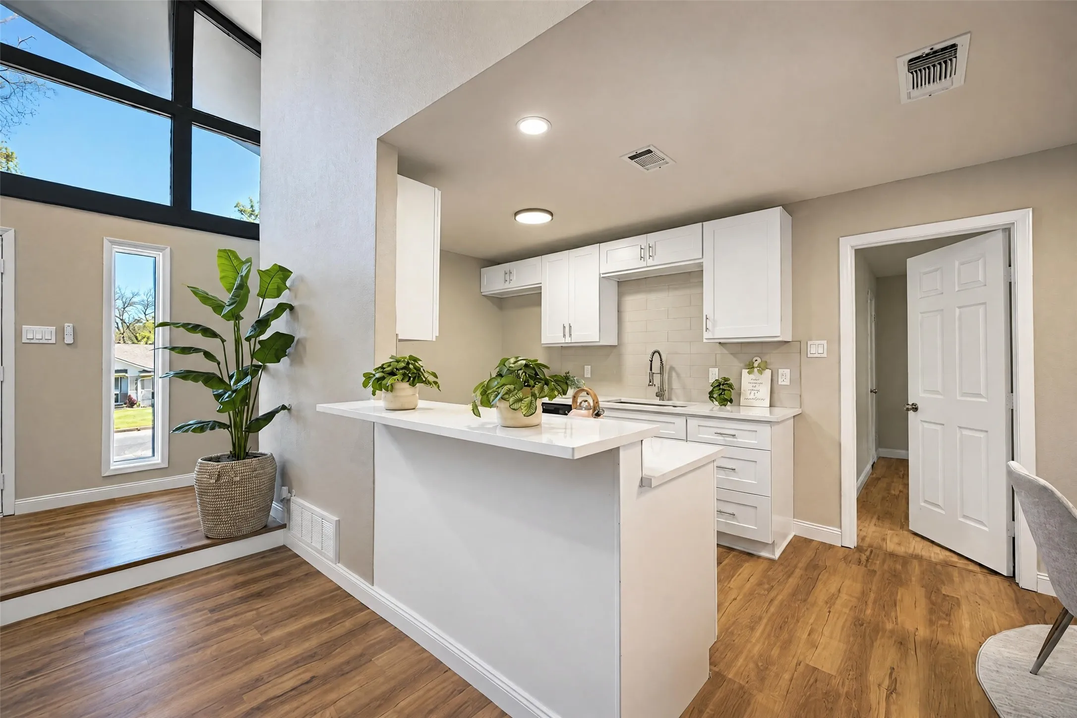 Kitchen featuring white shaker cabinetry, quartz countertops, a brick-pattern tile backsplash, wood-finish flooring, and expansive geometric windows