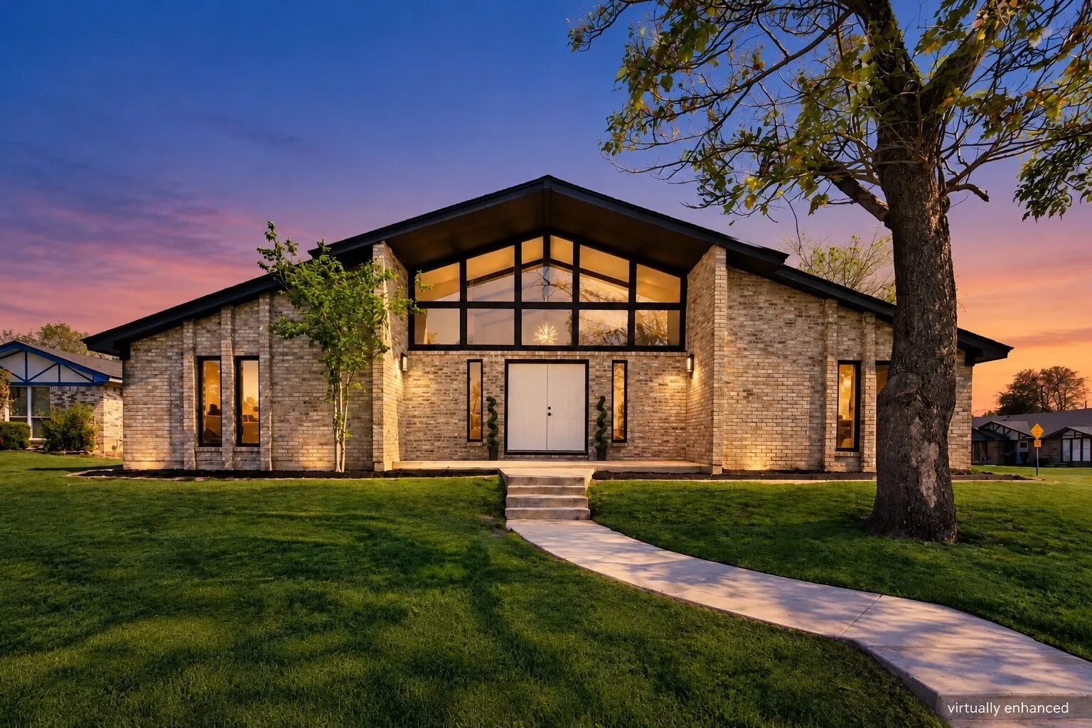 Mid-century modern exterior featuring light brick facade, expansive A-frame gabled roofline, floor-to-ceiling geometric windows, double-door entry, and stone walkway