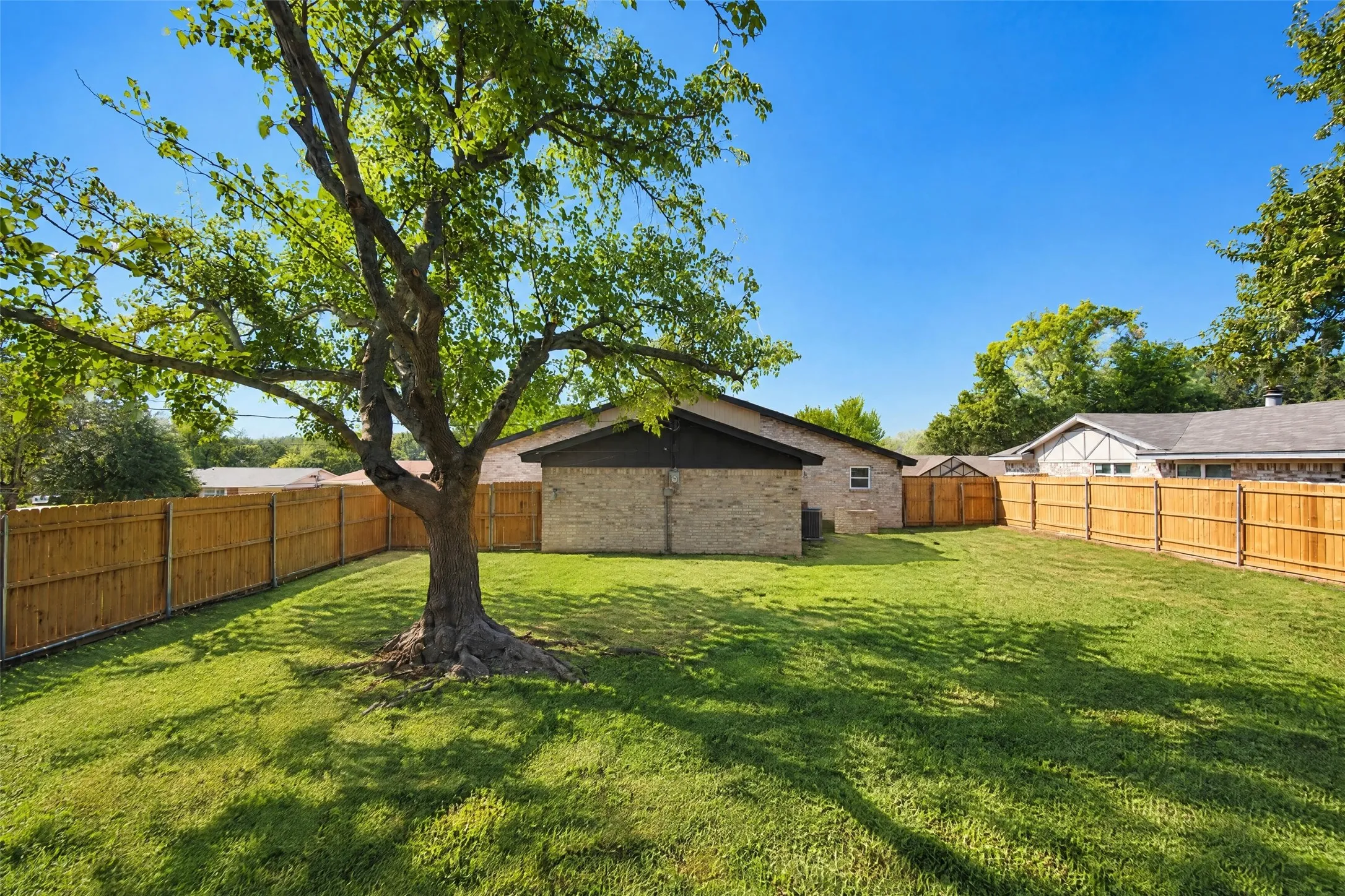 Backyard featuring a grass lawn, mature tree, and full-perimeter wood privacy fencing