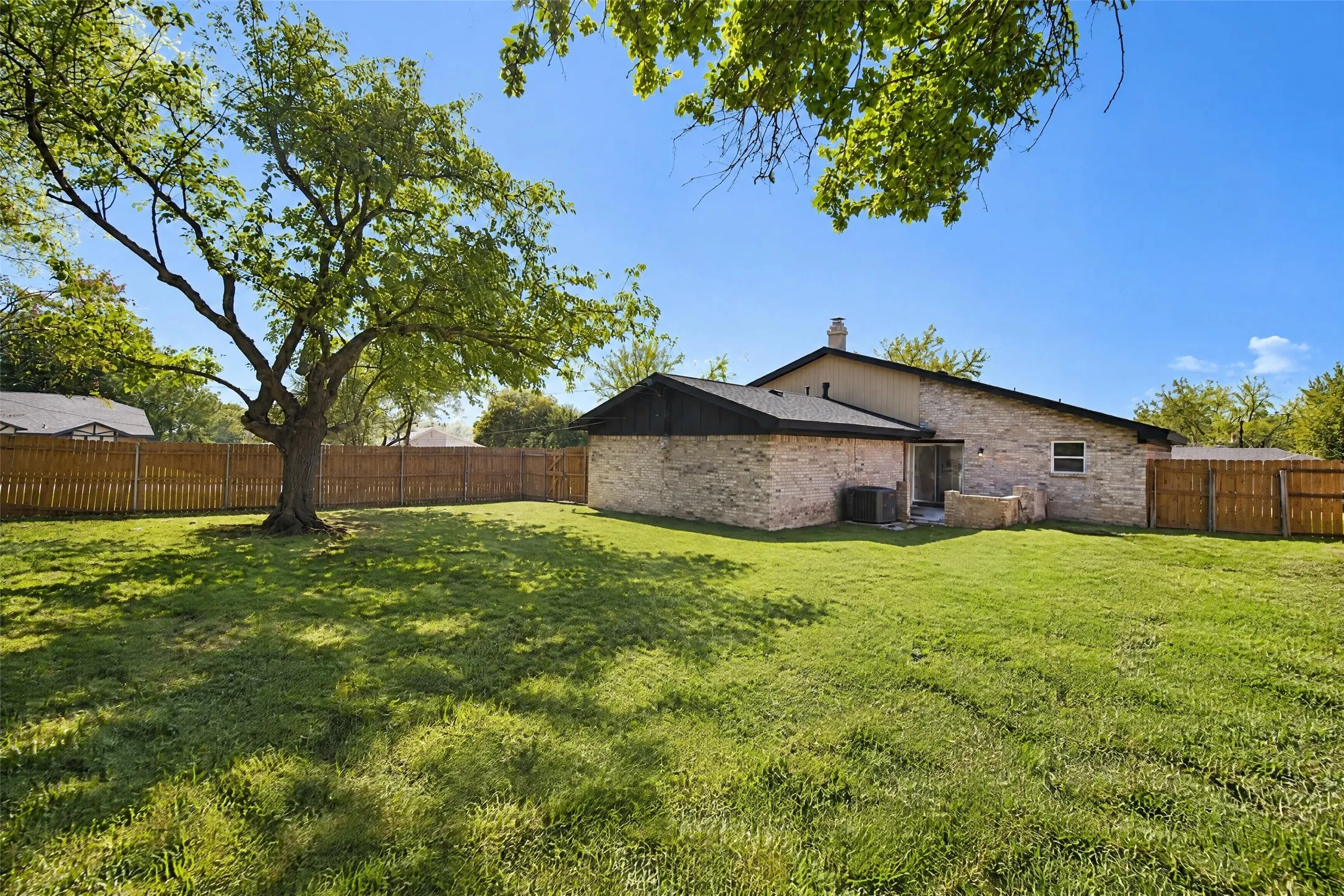 Backyard featuring a sprawling lawn, mature tree, stone veneer exterior, and a wood privacy fence