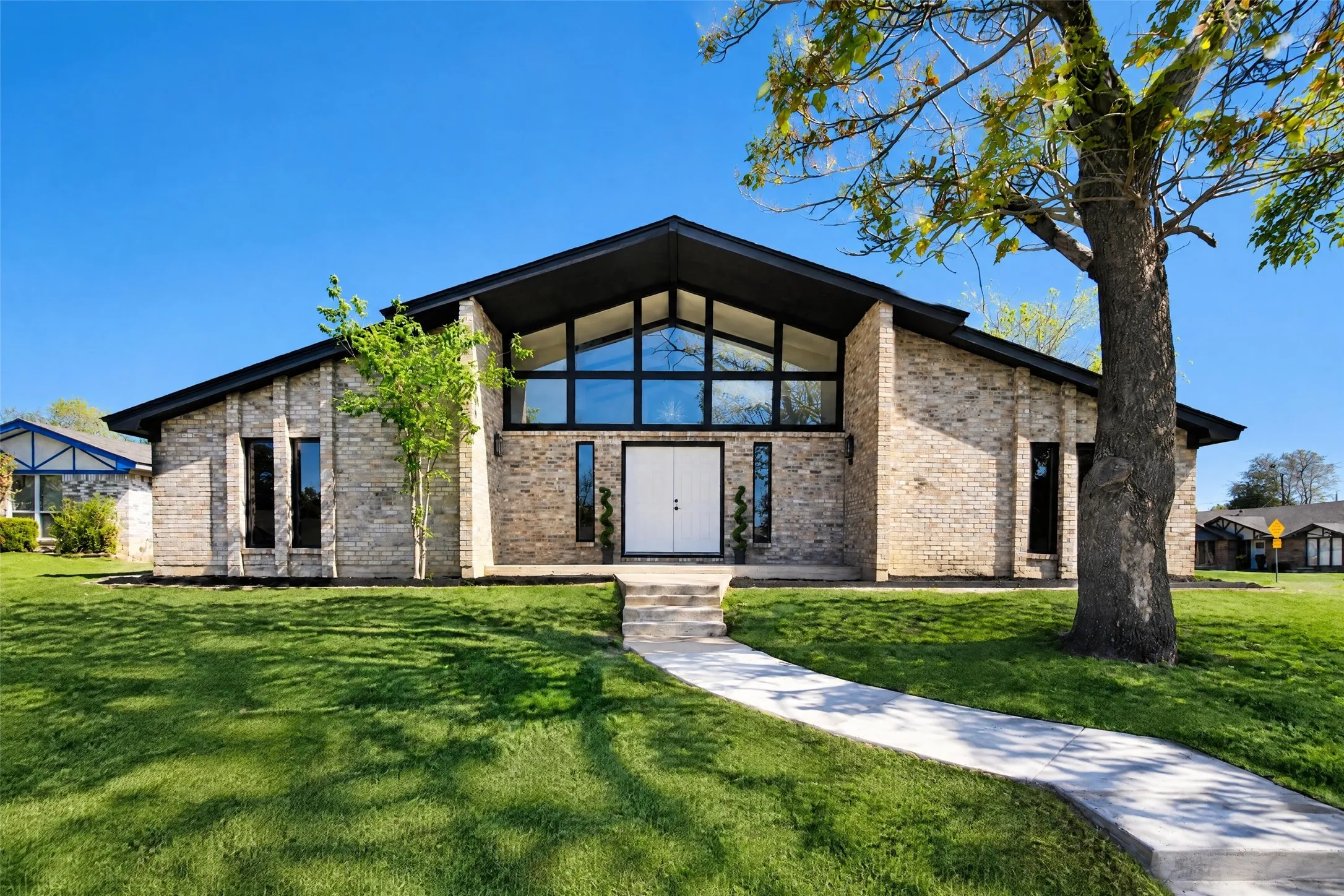 Brick exterior featuring a gabled roofline, expansive floor-to-ceiling multi-pane windows, double-door entryway, and stone-paved walkway