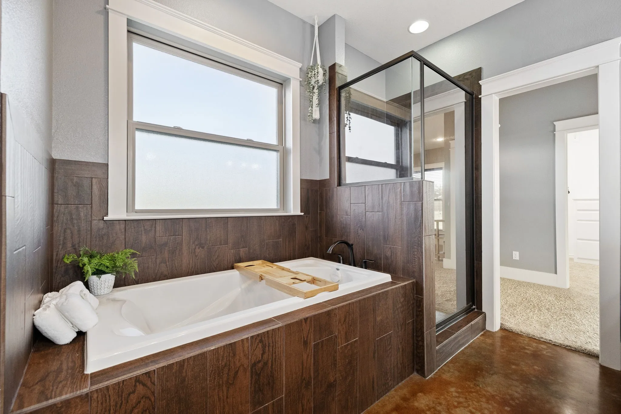 Built-in soaking tub with dark wood-finish tile surround, separate glass-enclosed shower, dark metal fixtures, and recessed lighting