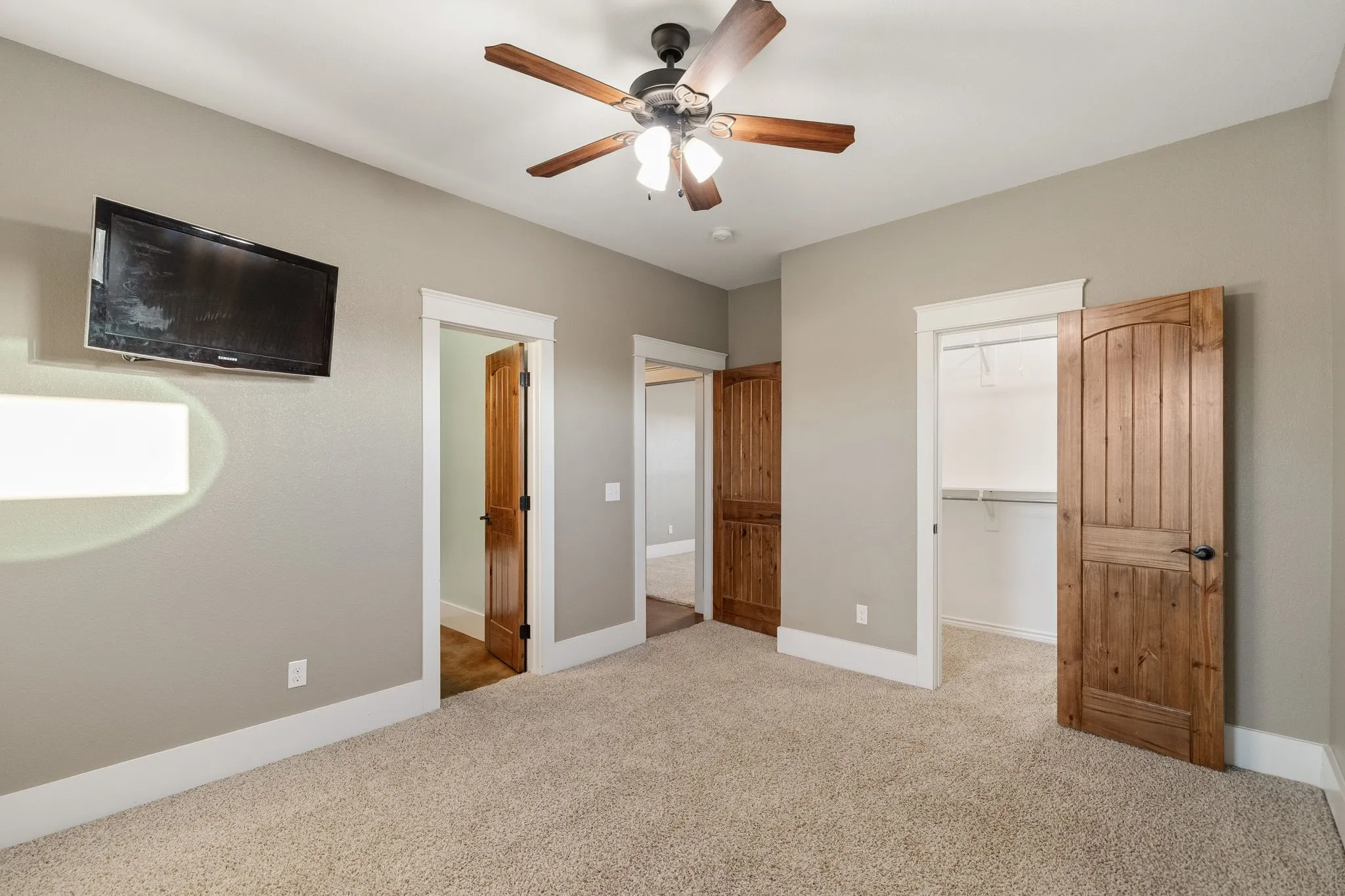 Neutral-toned room featuring plush wall-to-wall carpeting, wood-finish interior doors, a ceiling fan with integrated lighting, and a walk-in closet with built-in shelving