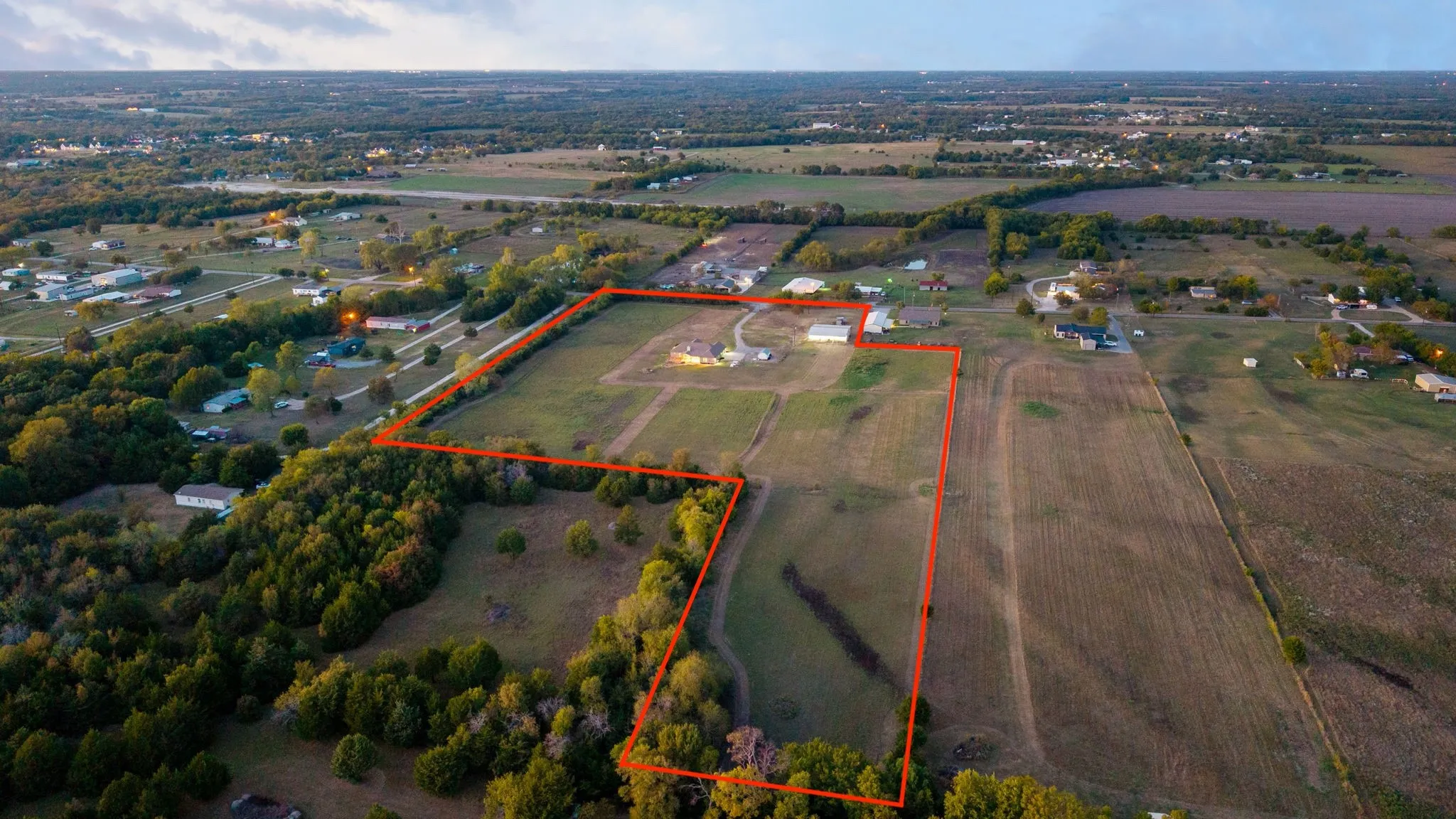 Aerial perspective of estimated sprawling acreage parcel featuring expansive pasture, mature tree clusters, a primary residential structure, and a detached outbuilding