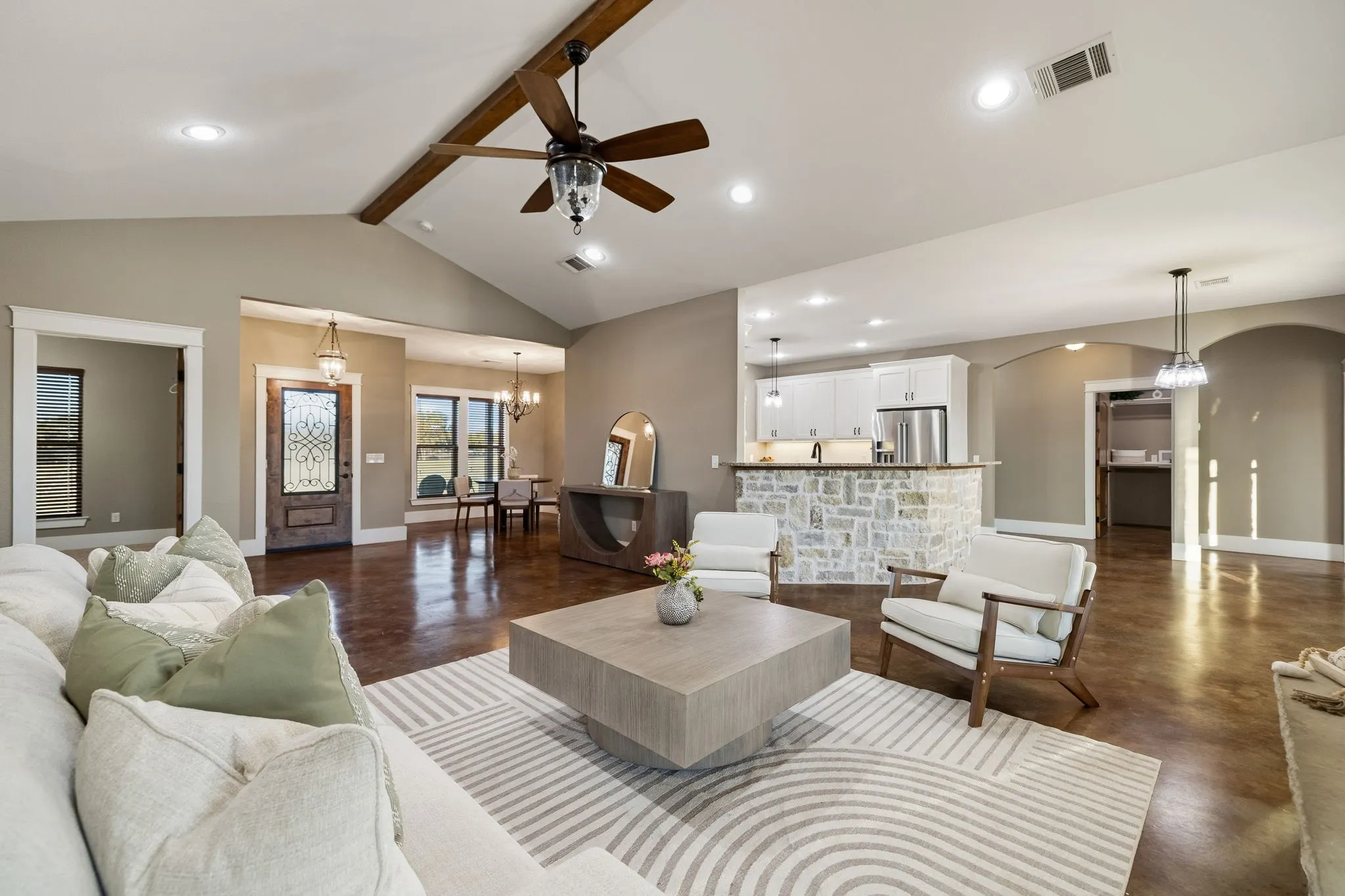 Vaulted ceilings with decorative wood beam, polished concrete flooring, stone-veneer kitchen island, recessed lighting, and ornate glass-paneled entry door