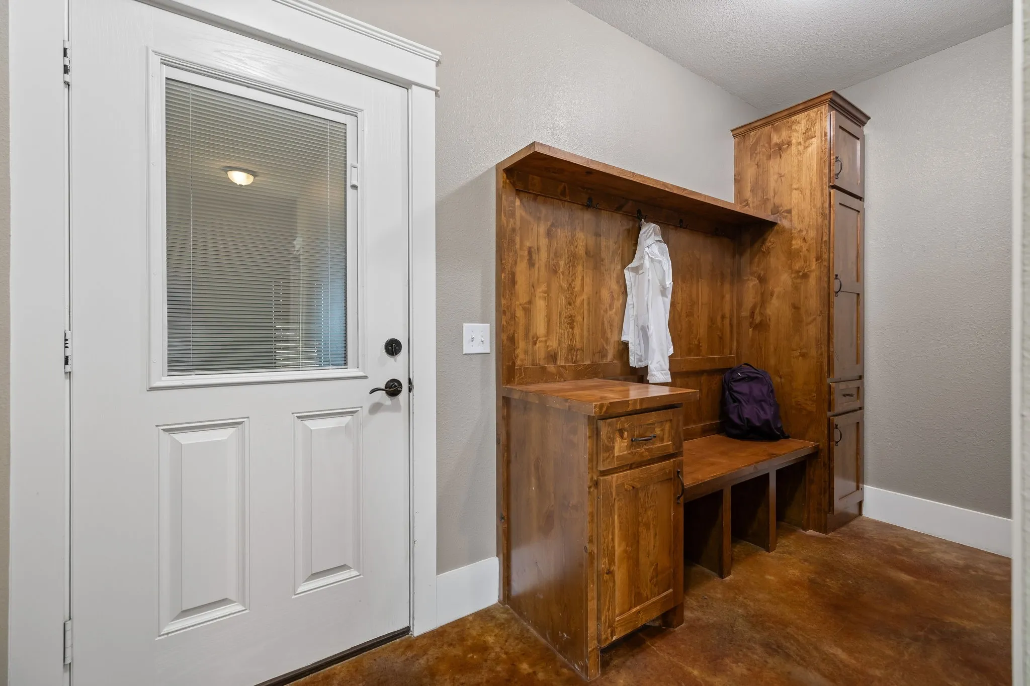 Built-in wood cabinetry featuring a bench seat, overhead shelving, and a tall storage tower, complemented by concrete flooring and a door with an integrated glass panel