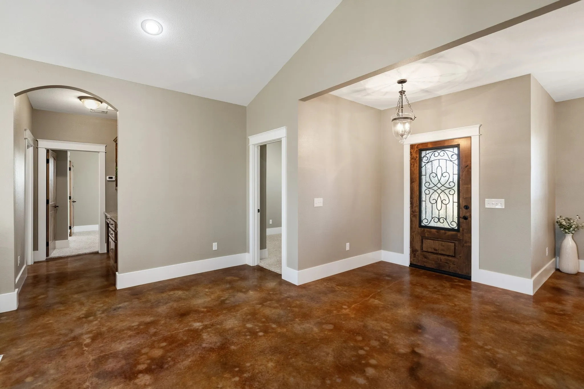 Interior space featuring stained concrete flooring, vaulted ceilings, an arched entryway, and an ornamental metal and wood front door with a decorative glass insert