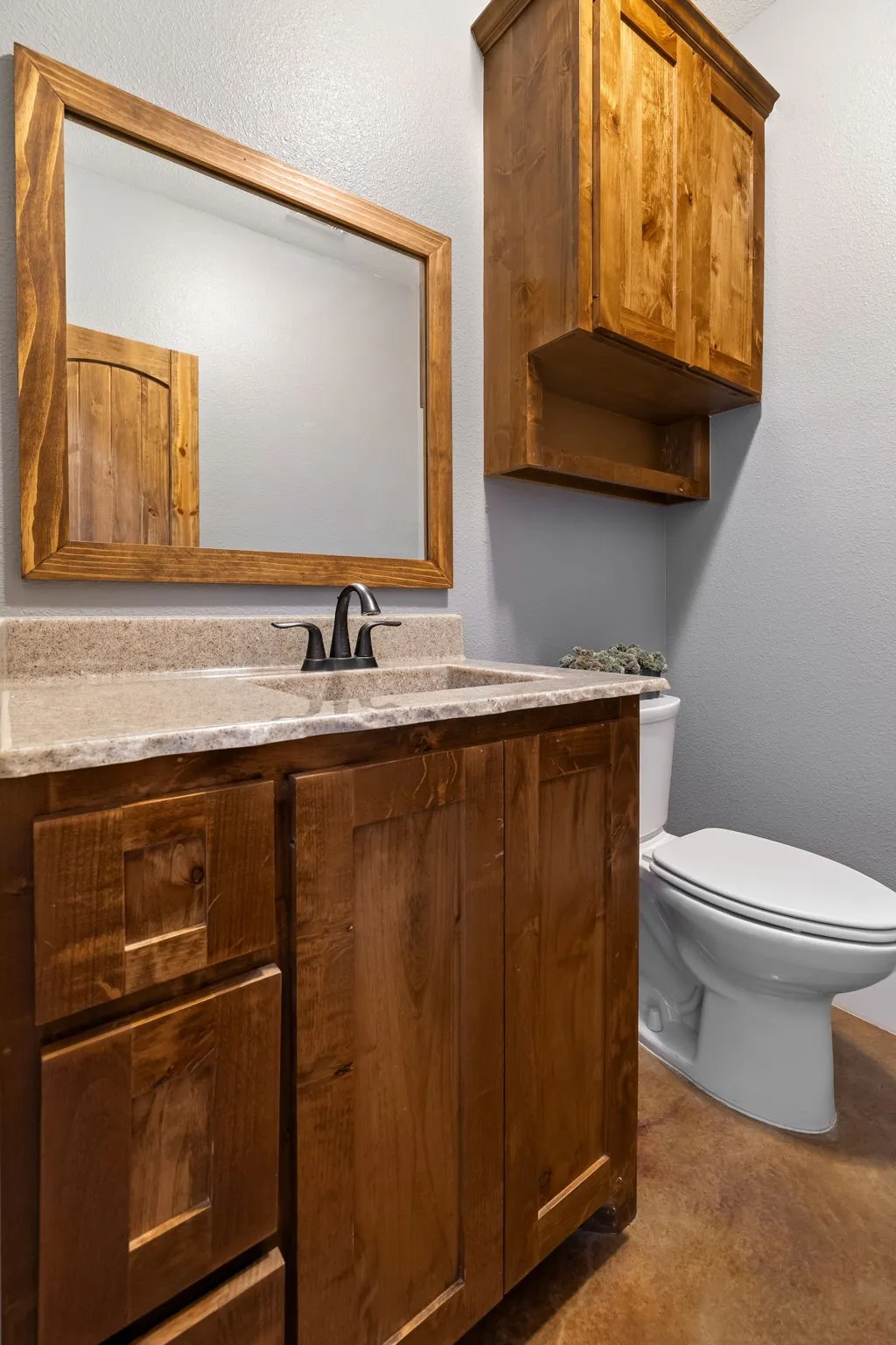Stained wood cabinetry, stone-finish vanity countertop, matching framed wall mirror, and dual-handle bronze-tone faucet