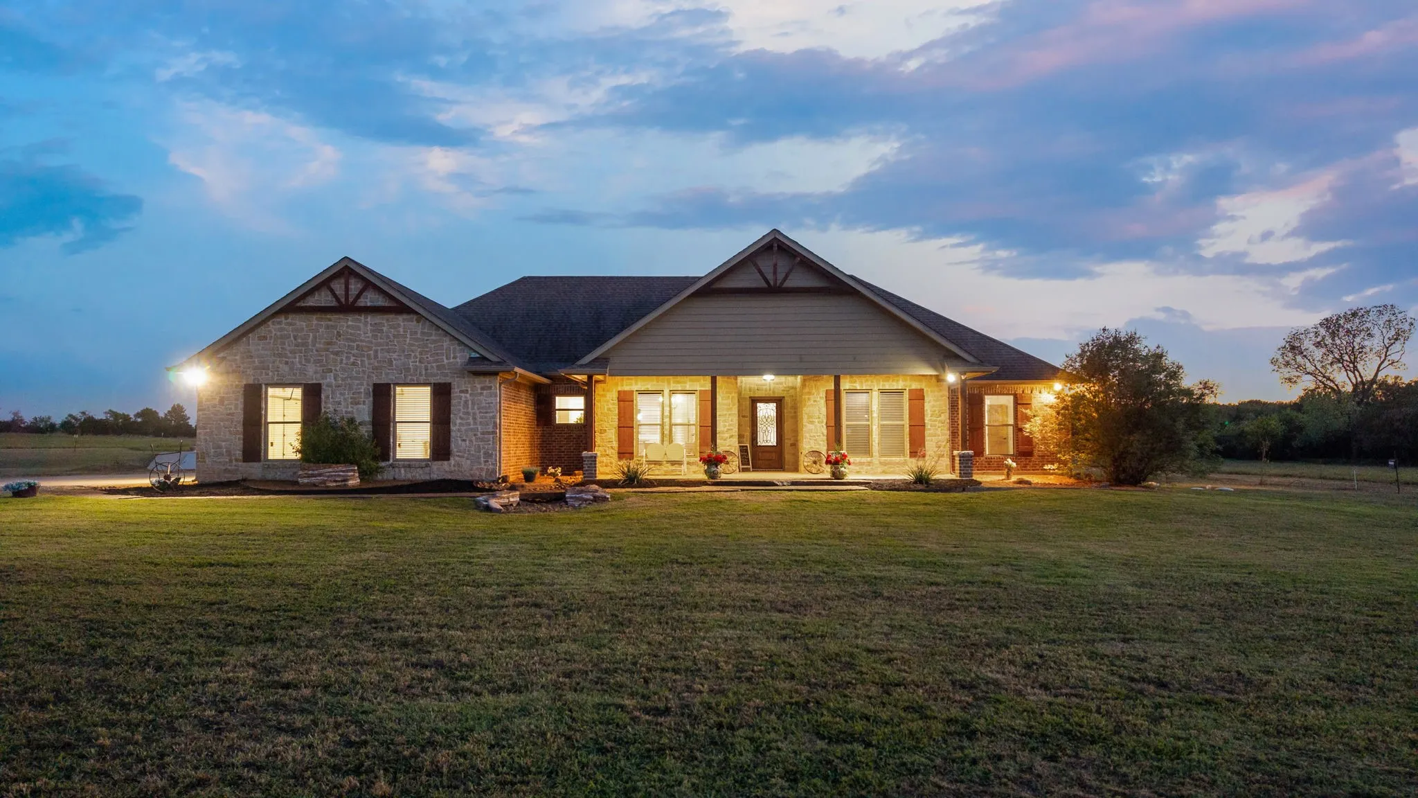 Single-story residence featuring stone and horizontal siding exterior, covered front porch, gabled roofline, decorative timber gable accents, and expansive lawn