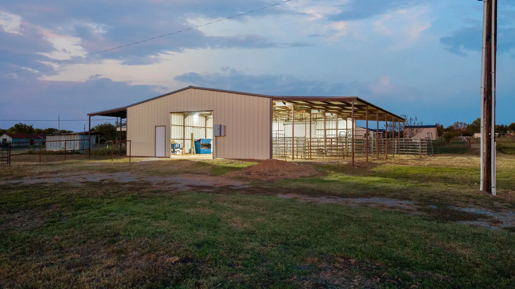 Metal-sided structure featuring a gable roof, integrated open-air stalls, and fenced perimeter