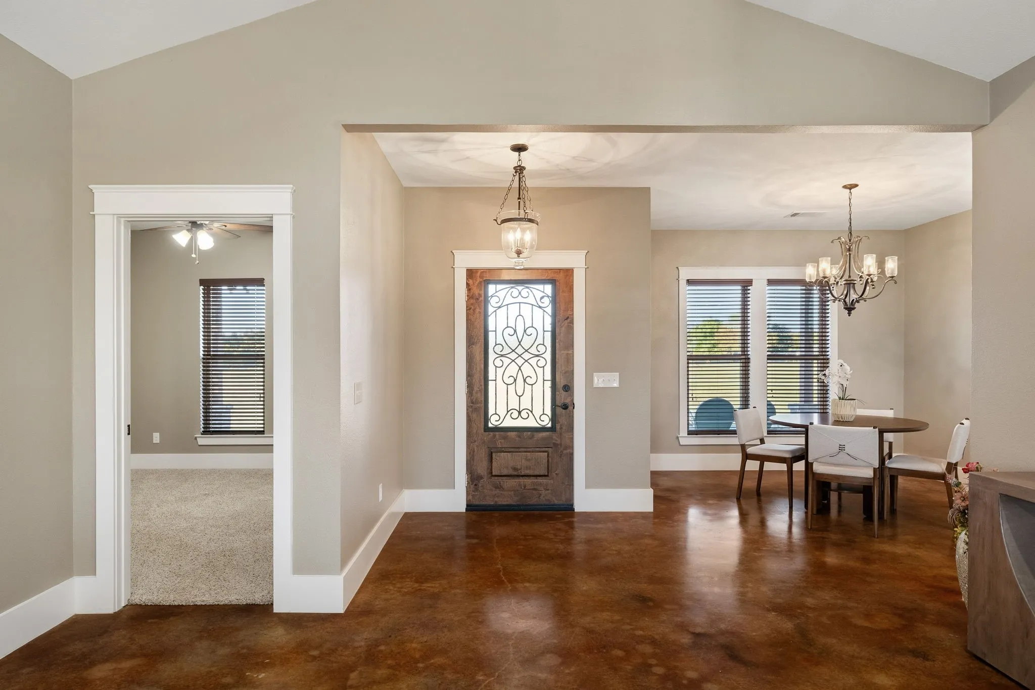 Entryway featuring high vaulted ceilings, stained concrete flooring, a decorative iron and wood front door, and polished chandeliers