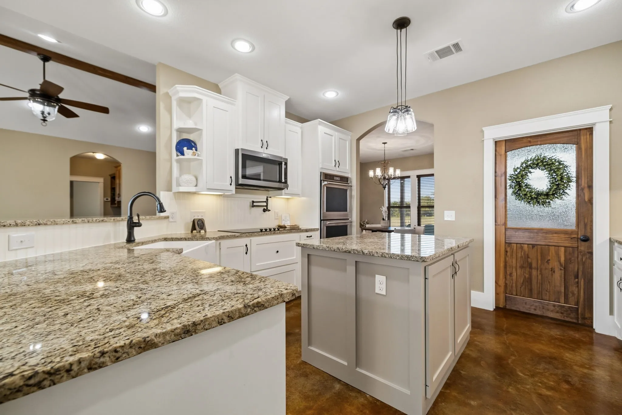 Kitchen featuring stone countertops, white cabinetry, integrated double wall ovens, a central island, and wood-finish flooring