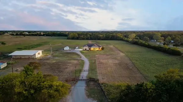 Aerial perspective featuring a multi-acre lot, single-story residence, detached workshop, gated entrance, and expansive open pastureland