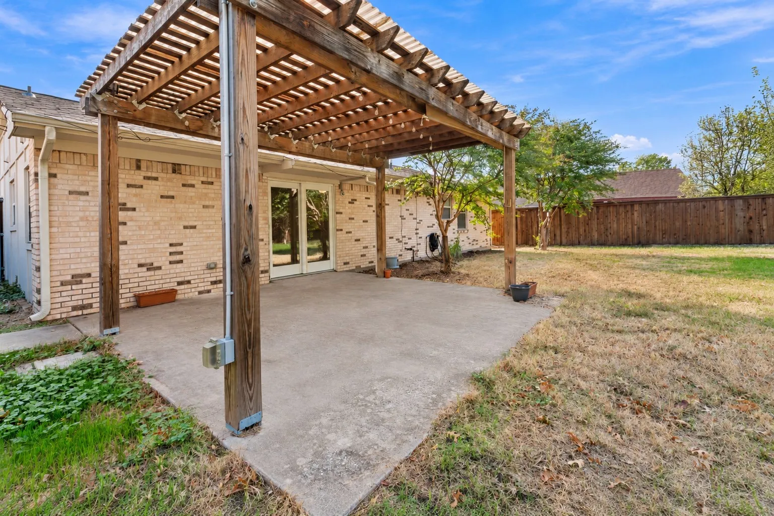 Backyard patio featuring a wood-beam pergola, concrete flooring, brick exterior siding, and a wooden privacy fence