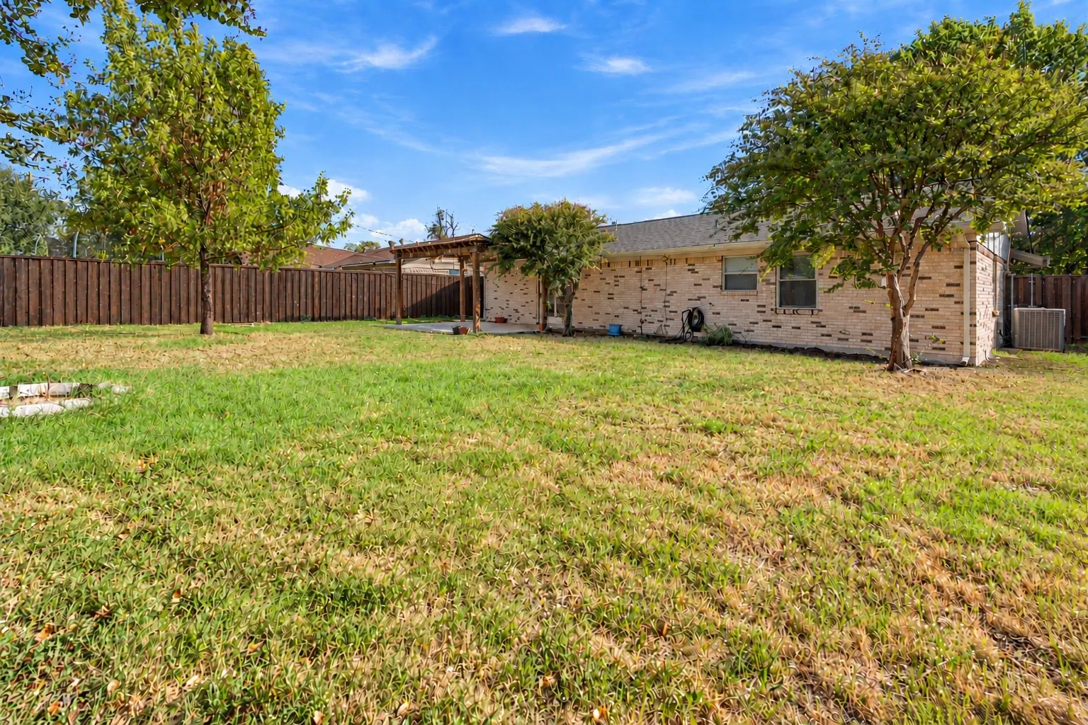 Brick exterior finish, wooden pergola, and expansive fenced yard with mature trees