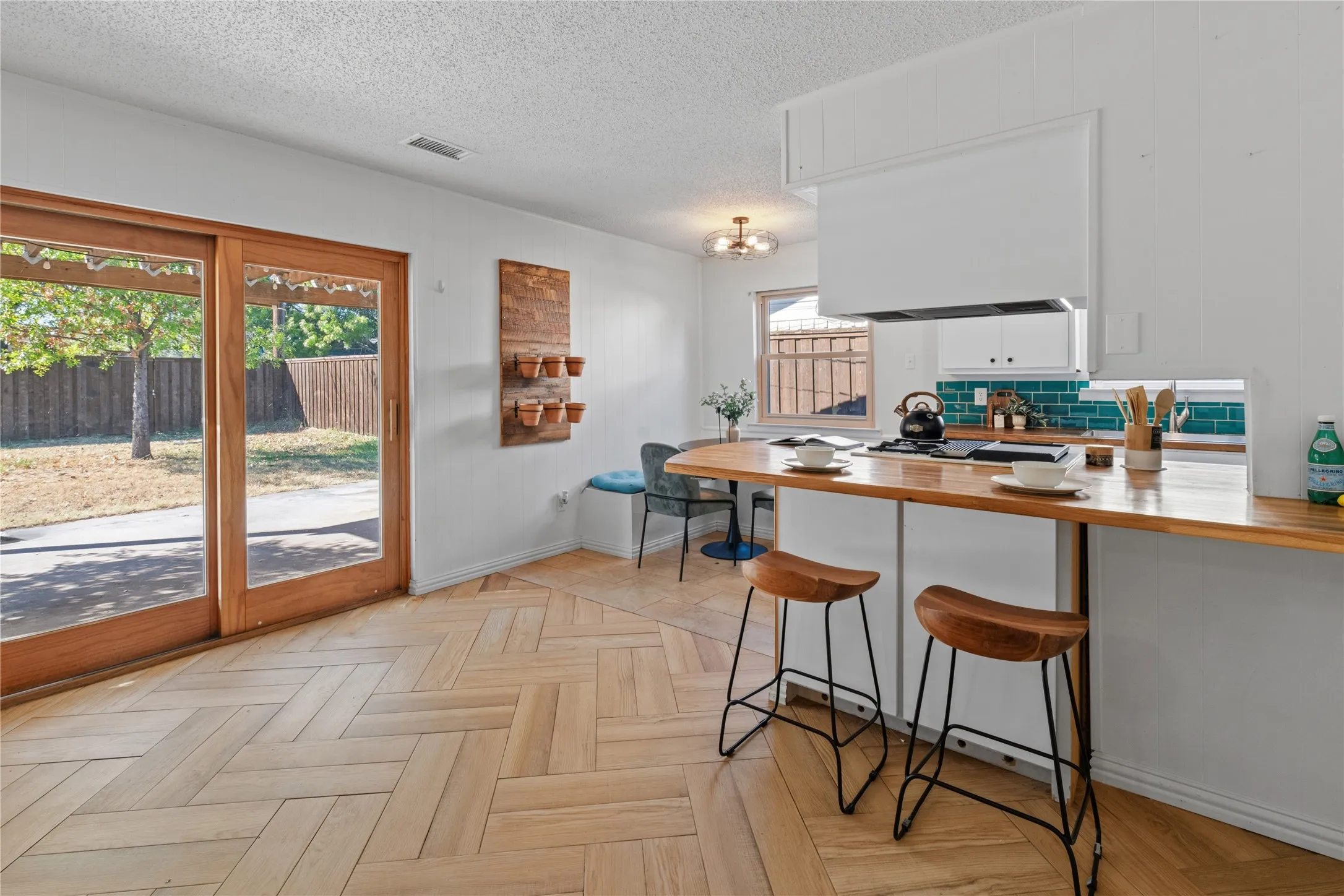 Herringbone-pattern wood-finish flooring, breakfast bar with wood countertop, teal tile backsplash, and wooden-frame sliding glass door