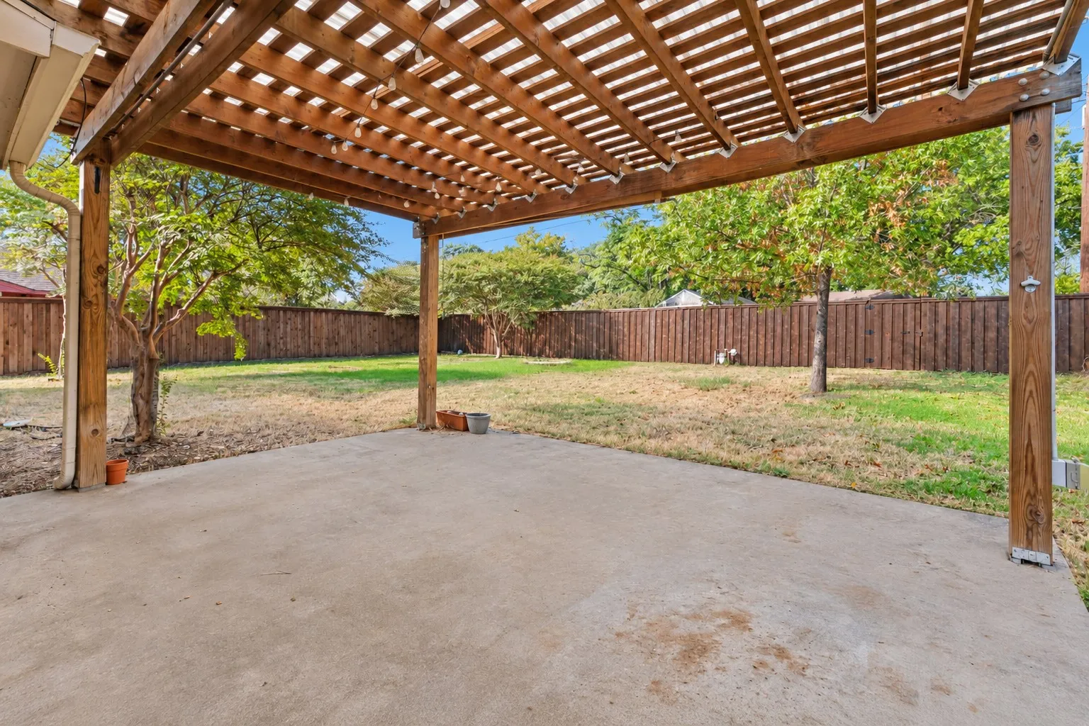 Covered patio featuring a wooden pergola, concrete flooring, and a fenced backyard with mature trees