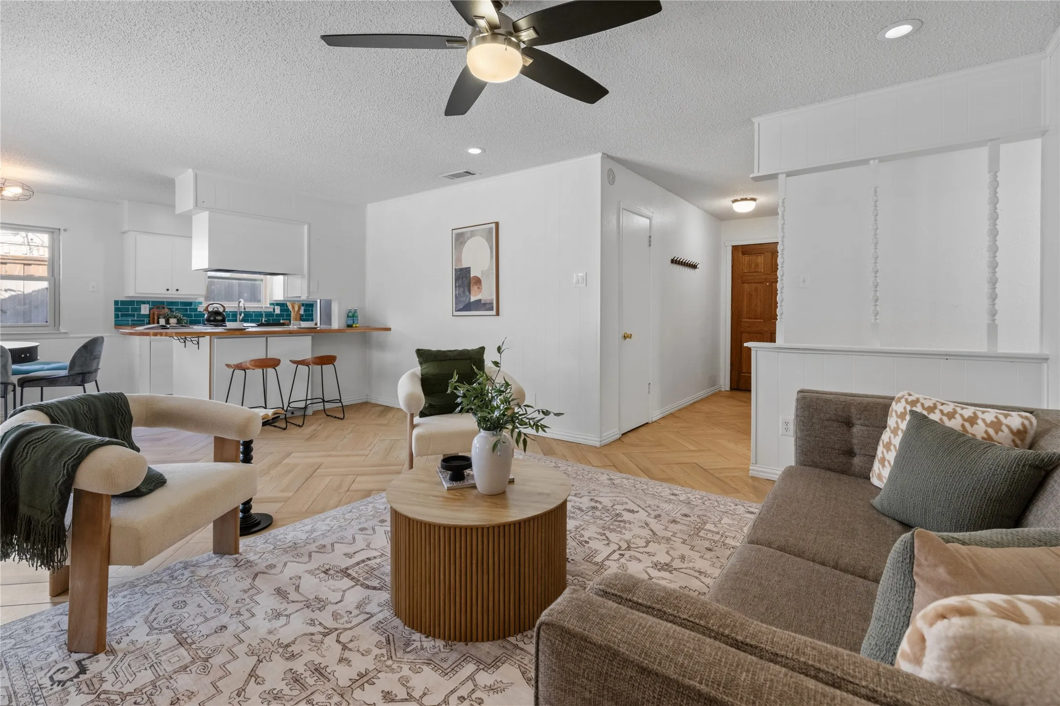 Open-concept space featuring herringbone-pattern wood-finish flooring, a kitchen breakfast bar with integrated cabinetry, ceiling-mounted paddle fan, and recessed lighting