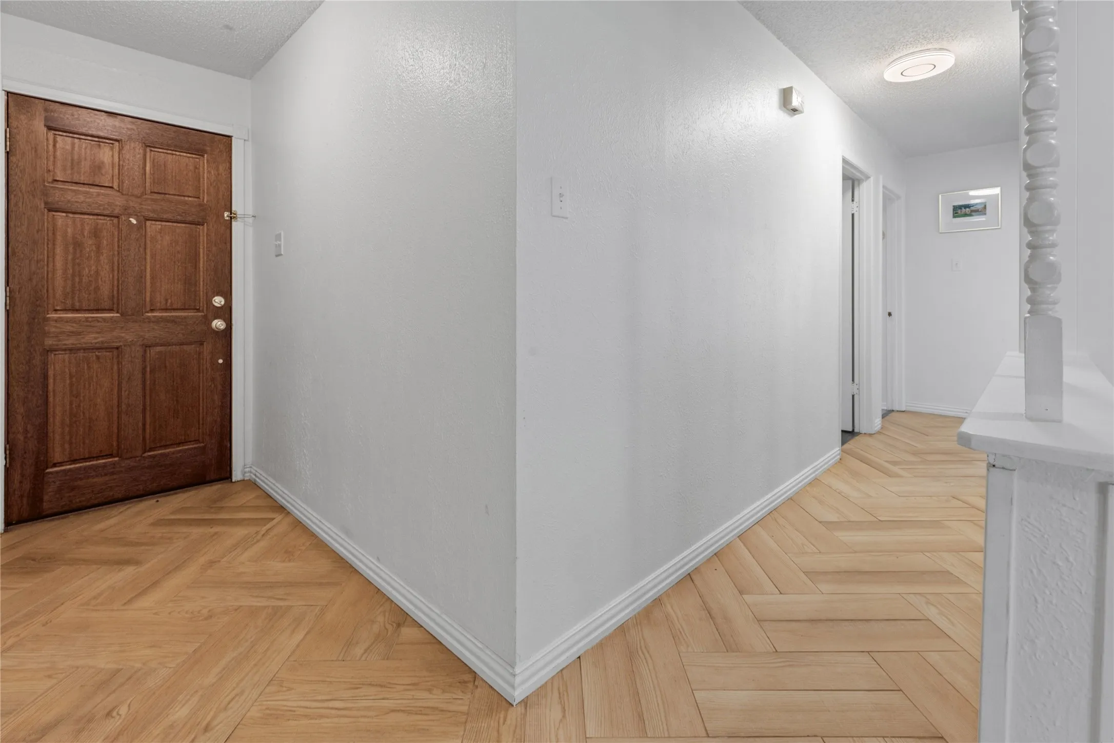 Entryway featuring a wood-finish door, herringbone-pattern wood-finish flooring, and a decorative white painted baluster