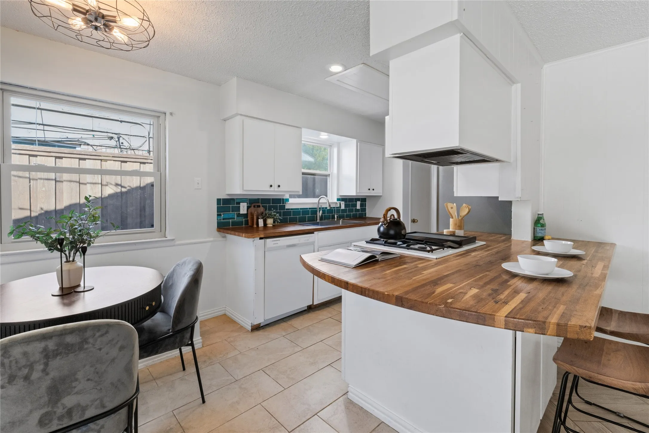 Kitchen featuring wood-finish countertops, white cabinetry, dark blue tile backsplash, gas cooktop, and tile flooring